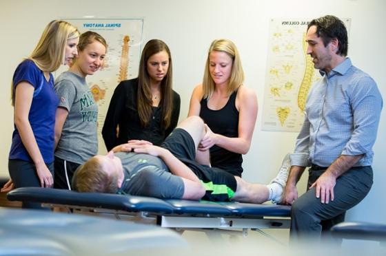 图为，在英国波胆网站，一名教师和四名理疗专业的女学生围绕在桌子上的一名病人周围，其中一名学生正在调整他的腿. 