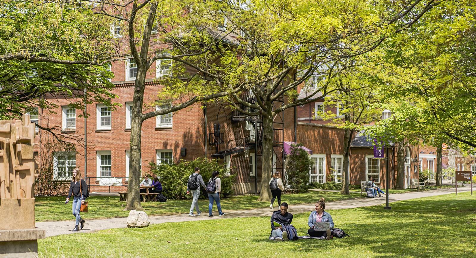 在一个阳光明媚的日子里，波胆网站的学生们步行去上课，坐在外面的学术广场上，周围是红砖教学楼和绿色植物