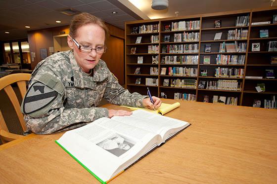图为一名身着制服的女军校学生在图书馆的桌子前工作