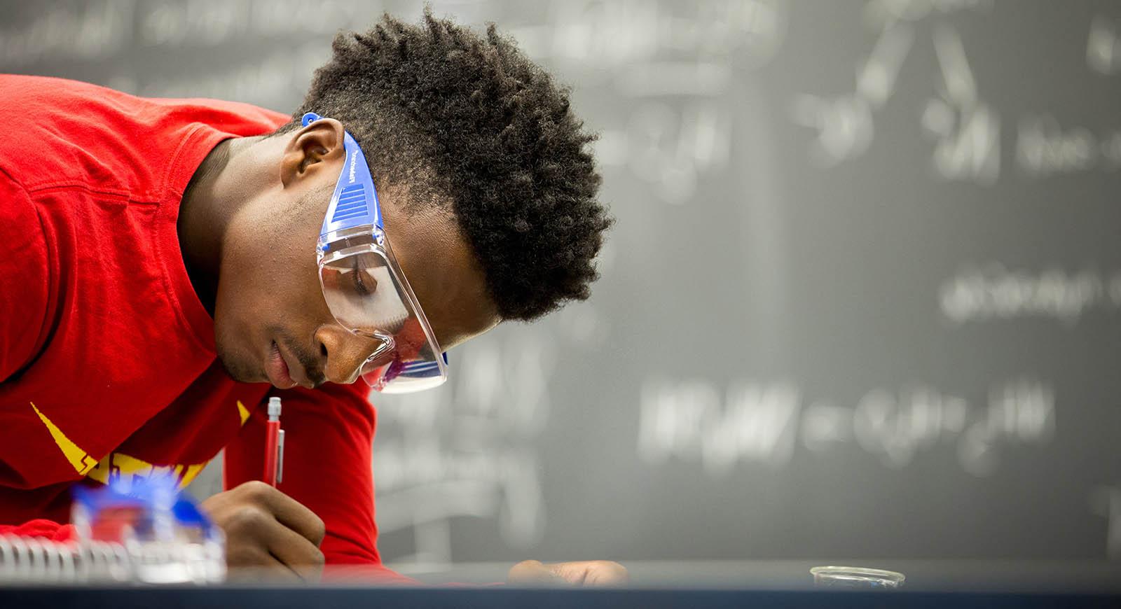 照片中的学生戴着护目镜，在实验室工作